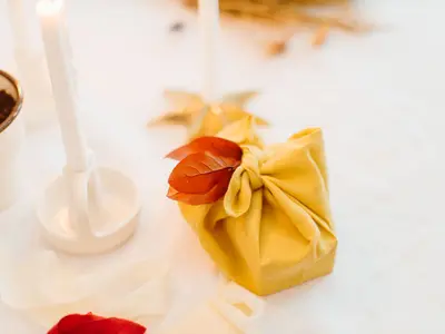 Prezent zawinięty w żółtą tkaninę w stylu furoshiki, ozdobiony jesiennym liściem