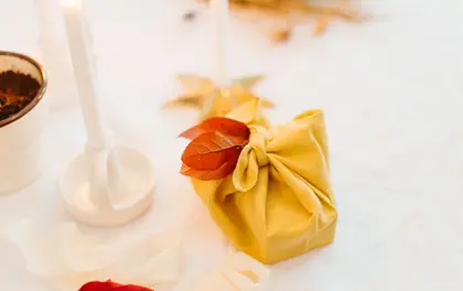 Prezent zawinięty w żółtą tkaninę w stylu furoshiki, ozdobiony jesiennym liściem